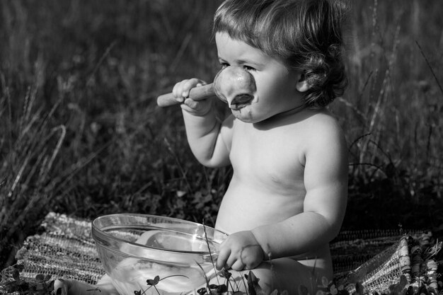 Bambino divertente che si siede sull'erba che tiene cucchiaio di legno per il cibo