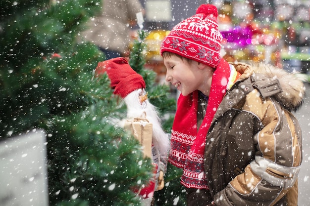 Bambino divertente con un giocattolo Babbo Natale al mercatino di Natale Ragazzino felice a Natale