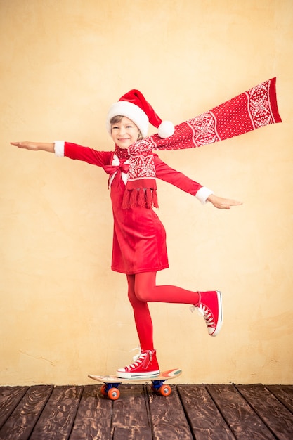 Bambino divertente della Santa con il pattino di guida della sciarpa di volo. Concetto di vacanza di Natale