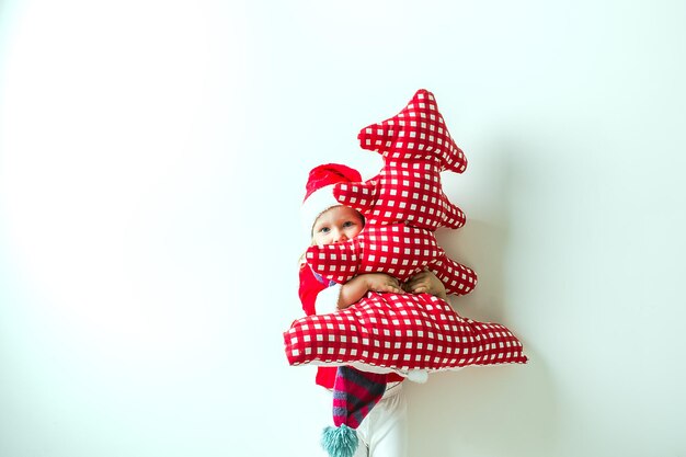 bambino divertente in un vestito di Babbo Natale abbraccia un albero di Natale in tessuto rosso