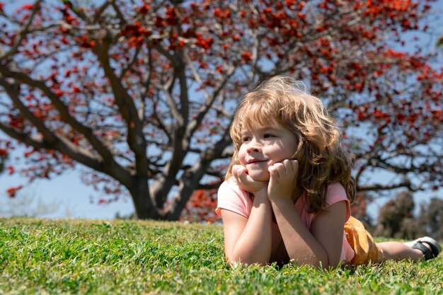 Bambino divertente nel parco naturale autunnale. Kid sdraiato sull'erba, cadono le foglie.