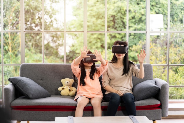 Bambino e donna con auricolare per realtà virtuale che sorridono mentre sono seduti sul divano in casa