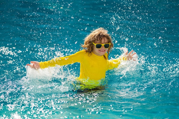 Bambino eccitato che spruzza acqua in piscina ragazzino che spruzza nell'acqua blu della piscina ragazzo carino s