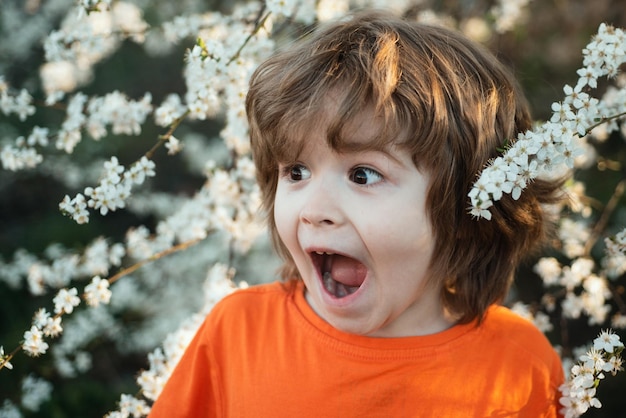 Bambino eccitato nell'albero in fiore nel parco primaverile ragazzo felice giardino fiorito all'aperto