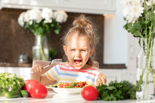 bambino emotivo si diverte a mangiare sano insalata cucina verdure fresche a tavola pasto Nutrizione e Vegan