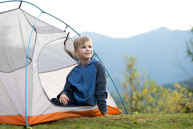 Bambino escursionista che riposa in una tenda turistica in un campeggio di montagna godendo della vista della bellissima natura estiva.