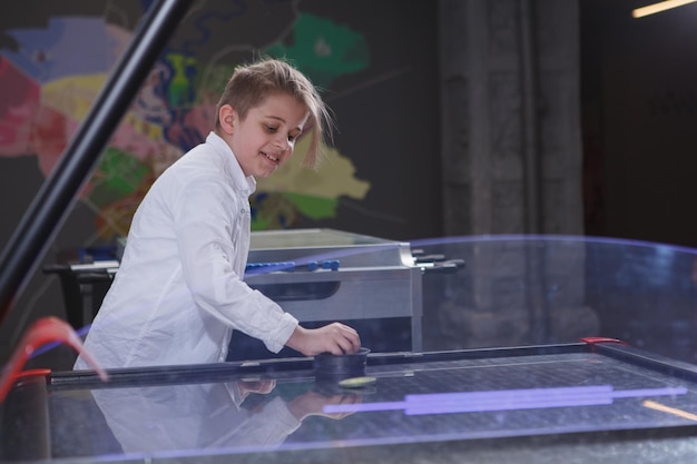 Bambino felice adorabile che sorride giocando lo spazio della copia di air hockey