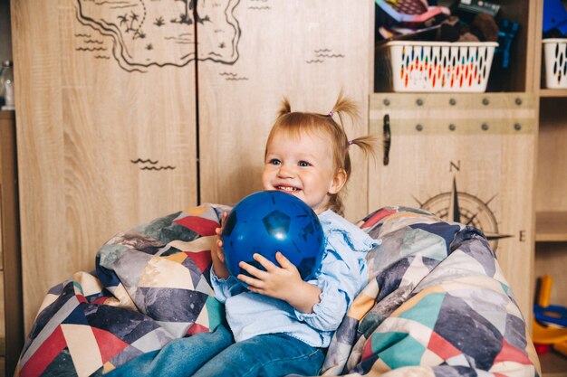 Bambino felice, bambina che gioca con una palla mentre è seduto su una sedia morbida. bambino gioca con una palla.