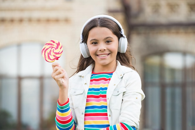 Bambino felice che canta caramelle dolci microfono Infanzia felice Cuffie per bambini con lecca lecca in mano Bambino felice con caramelle all'aperto che si divertono Calorie ed energia La studentessa merita il dessert Dolce remix