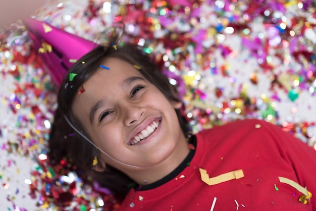 Bambino felice che celebra la festa con i coriandoli che soffia mentre giace sul pavimento