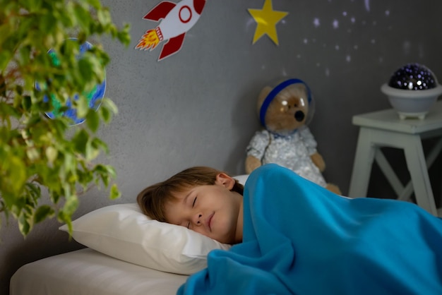 Bambino felice che dorme con un razzo giocattolo e un orsacchiotto. Il bambino finge di essere un astronauta. Immaginazione e concetto di sogno dei bambini