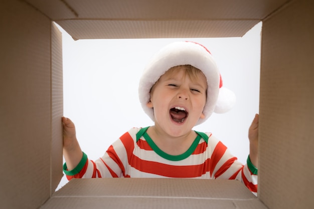 Bambino felice che esamina la scatola. Il neonato sorpreso divertente disimballa il contenitore di regalo di Natale. Concetto di vacanza di Natale. Inquadratura dal basso.