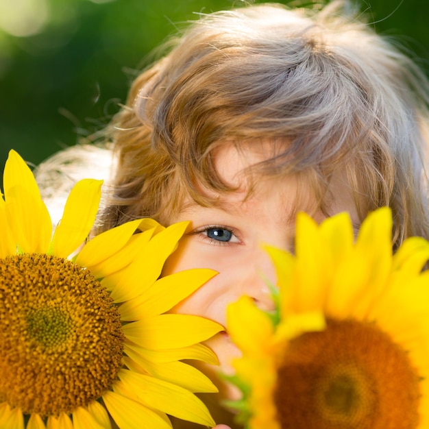 Bambino felice che gioca con i girasoli all'aperto nel parco di primavera