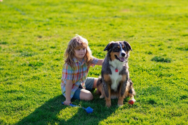 Bambino felice che gioca con il cane nel campo di erba verde Bambino carino con un cucciolo di cane estivo all'aperto