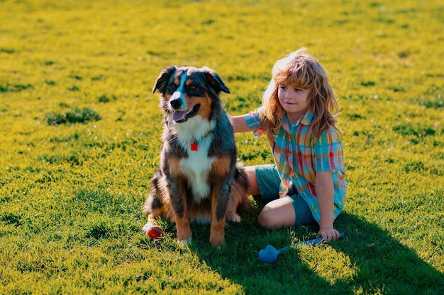 Bambino felice che gioca con il cane nel campo di erba verde Bambino carino con un cucciolo di cane estivo all'aperto