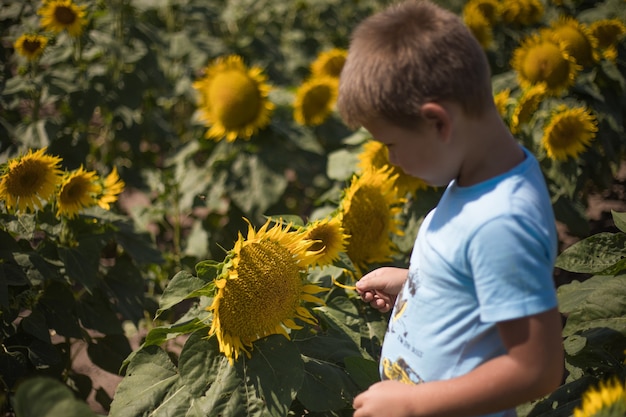 Bambino felice che gioca con il girasole all'aperto. Kid divertirsi nel campo di primavera verde sullo sfondo del cielo blu. Concetto di stile di vita sano e attivo