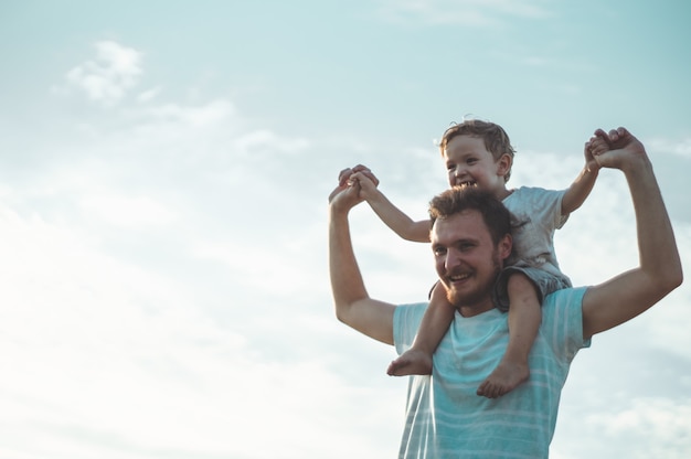 Bambino felice che gioca con il padre. Papà e figlio all'aperto. Padre che porta il bambino sulla schiena. Famiglia felice nel campo estivo.