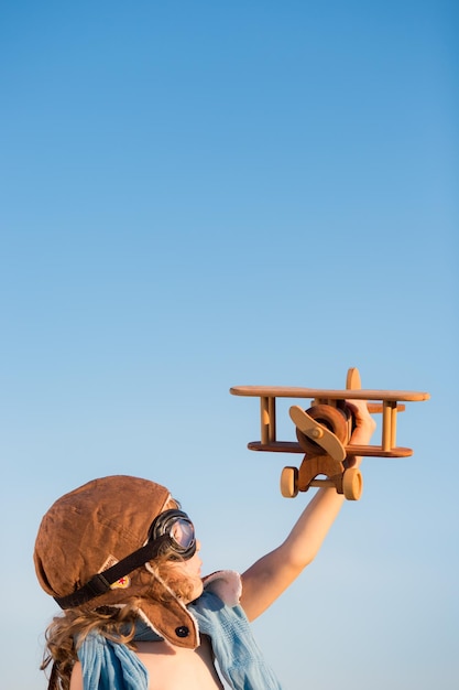 Bambino felice che gioca con l'aeroplano giocattolo su sfondo blu cielo estivo