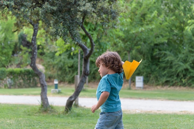 Bambino felice che gioca con l'aeroplano giocattolo sullo sfondo del cielo estivo al tramonto