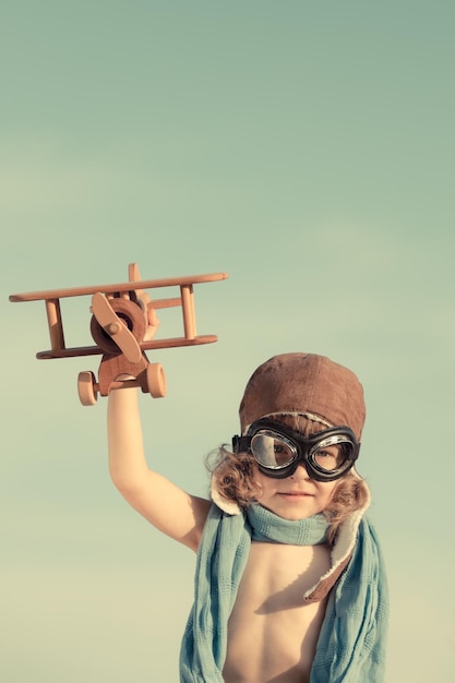 Bambino felice che gioca con l'aeroplano giocattolo sullo sfondo del cielo estivo Concetto di viaggio