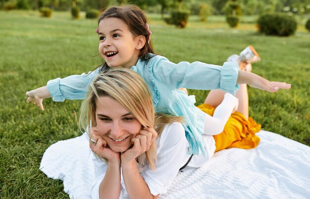 Bambino felice che gioca con la bella madre nel parco Bella giovane donna e sua figlia che si rilassano sull'erba verde Mamma e bambina condividono l'amore Buona festa della mamma Maternità e infanzia