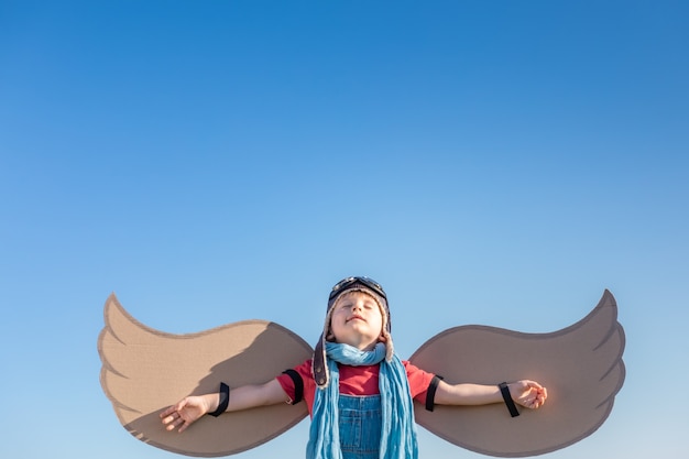Bambino felice che gioca con le ali del giocattolo contro il fondo del cielo blu