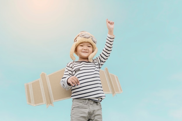 Bambino felice che gioca con le ali del giocattolo contro il fondo del cielo di estate.