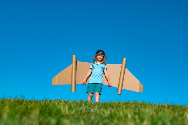 Bambino felice che gioca con le ali del giocattolo sullo sfondo del cielo estivo Leader di successo per bambini e concetto di vincitore