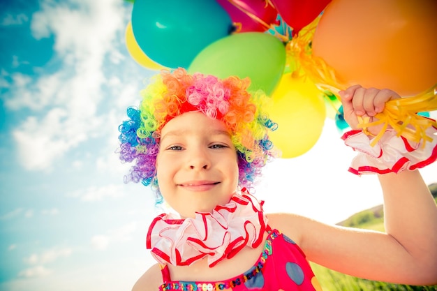 Bambino felice che gioca con palloncini colorati giocattolo all'aperto. Bambino sorridente che si diverte nel campo verde della primavera su sfondo blu del cielo. Concetto di libertà