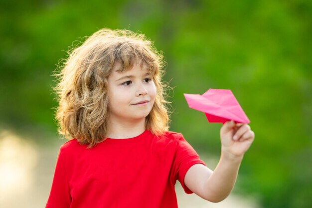 Bambino felice che gioca con un aeroplano di carta bambino carino che lancia un aeroplano di carta nel parco in una giornata estiva felice