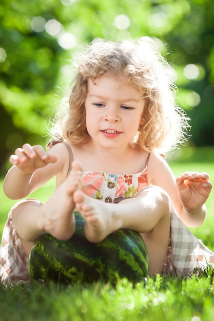 Bambino felice che gioca con una grande anguria sull'erba verde nel parco estivo Concetto di alimentazione sana