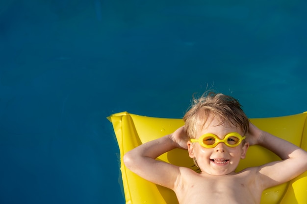 Bambino felice che nuota in piscina. Kid divertirsi in vacanza estiva. Concetto di stile di vita sano