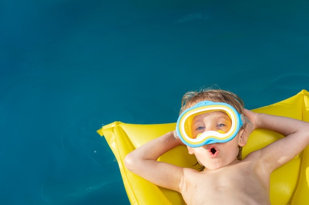 Bambino felice che nuota in piscina. Kid divertirsi in vacanza estiva. Concetto di stile di vita sano