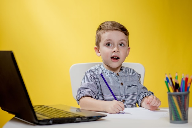 Bambino felice che per mezzo del computer portatile digitale che fa i compiti su priorità bassa gialla.