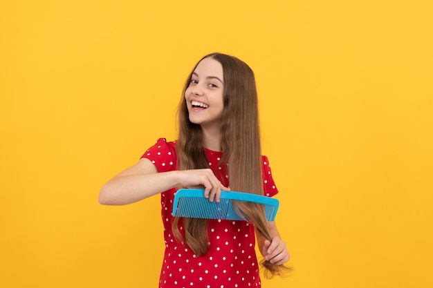 Bambino felice che pettina i capelli lunghi sulla cura dei capelli del fondo giallo