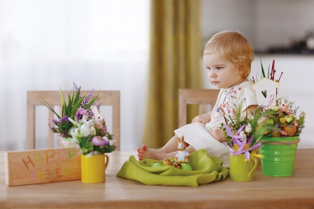 Bambino felice che si siede al tavolo e che tiene l&#39;uovo di Pasqua