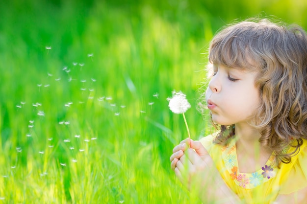 bambino felice che soffia fiore di tarassaco all'aperto ragazza che si diverte nel parco di primavera spring