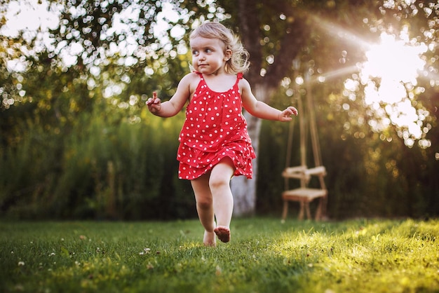 Bambino felice che sorride una bambina che corre in giardino al tramonto all'aperto a piedi nudi