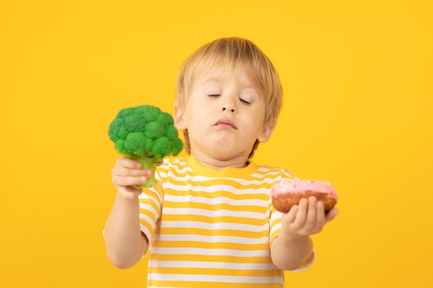 Bambino felice che tiene ciambella e broccoli