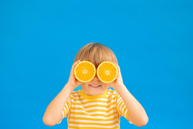 Bambino felice che tiene fette di frutta arancione come occhiali da sole