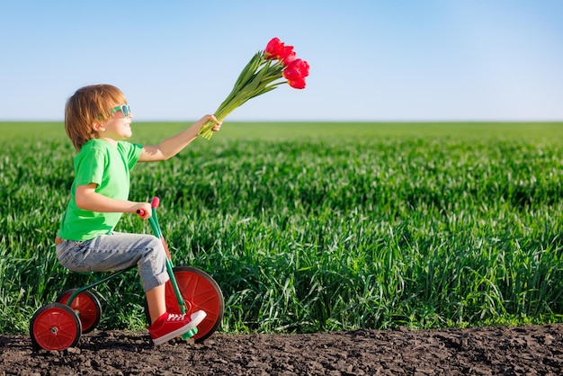 Bambino felice che tiene i fiori su sfondo blu del cielo