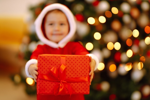 Bambino felice che tiene il contenitore di regalo rosso sulle luci di sfondo.