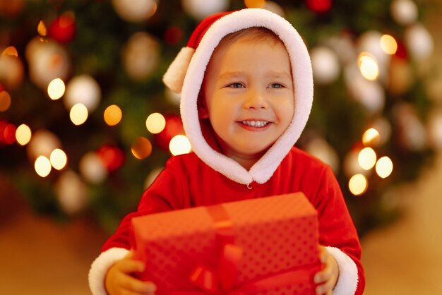 Bambino felice che tiene il contenitore di regalo rosso sulle luci di sfondo.