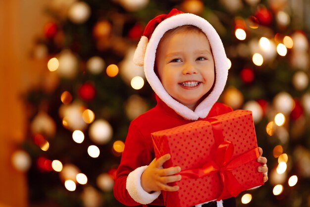 Bambino felice che tiene il contenitore di regalo rosso sulle luci di sfondo.