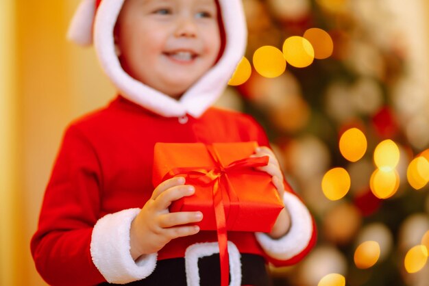 Bambino felice che tiene il contenitore di regalo rosso sulle luci di sfondo.