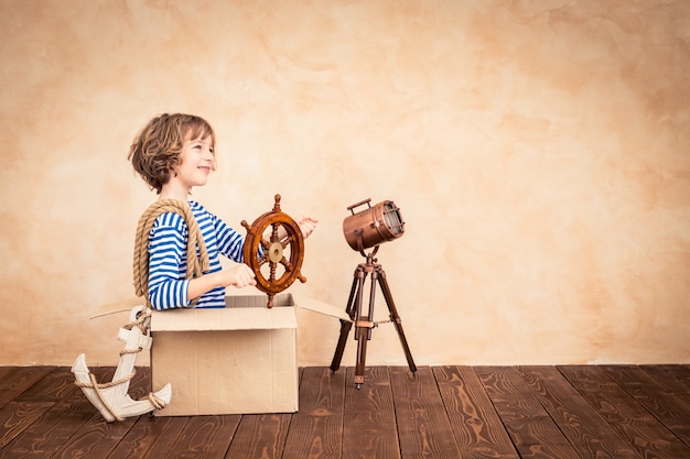 bambino felice che tiene il timone seduto su una valigia vintage con un focus su uno sfondo a tema marinaio