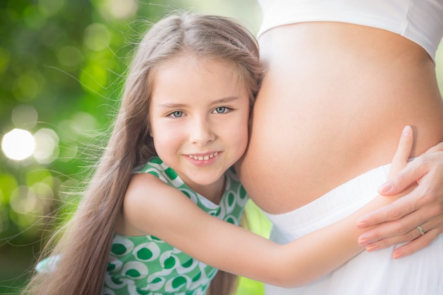 bambino felice che tiene la pancia della famiglia della donna incinta che si diverte all'aperto nella festa della mamma del parco di primavera spring