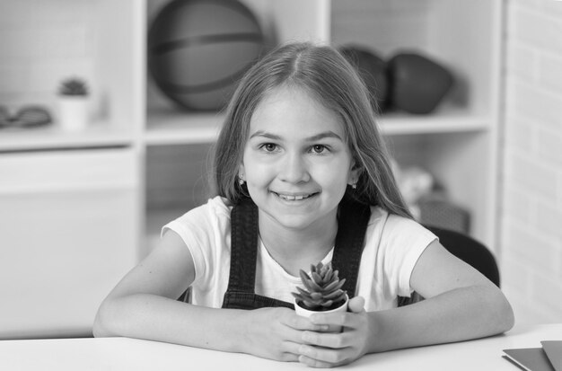 Bambino felice che tiene pianta in vaso in aula scolastica sulla semina della lezione