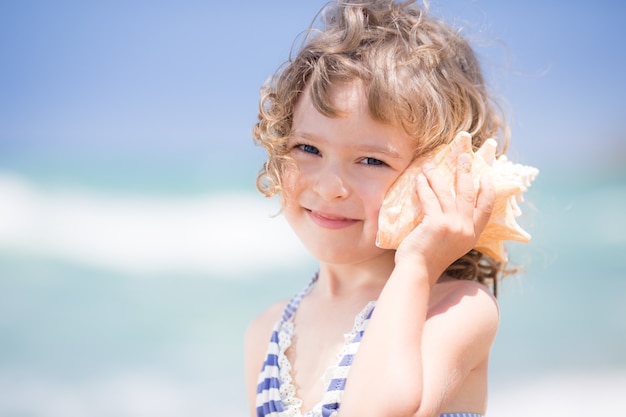 Bambino felice con conchiglia in spiaggia Vacanze estive concept