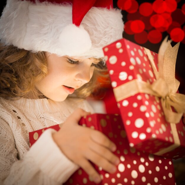 Bambino felice con il cappello di Babbo Natale che apre la confezione regalo di Natale